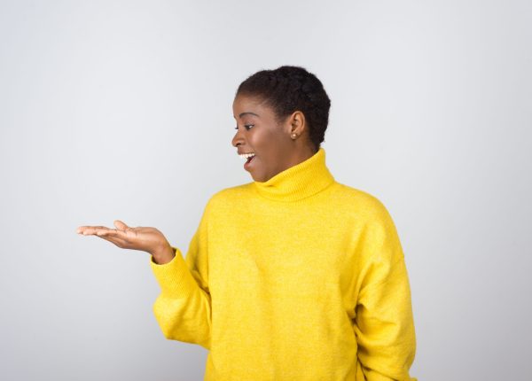 Surprised woman looking at copy space on palm. Beautiful happy young African American woman gesturing showing something on palm isolated on white background. Advertisement concept